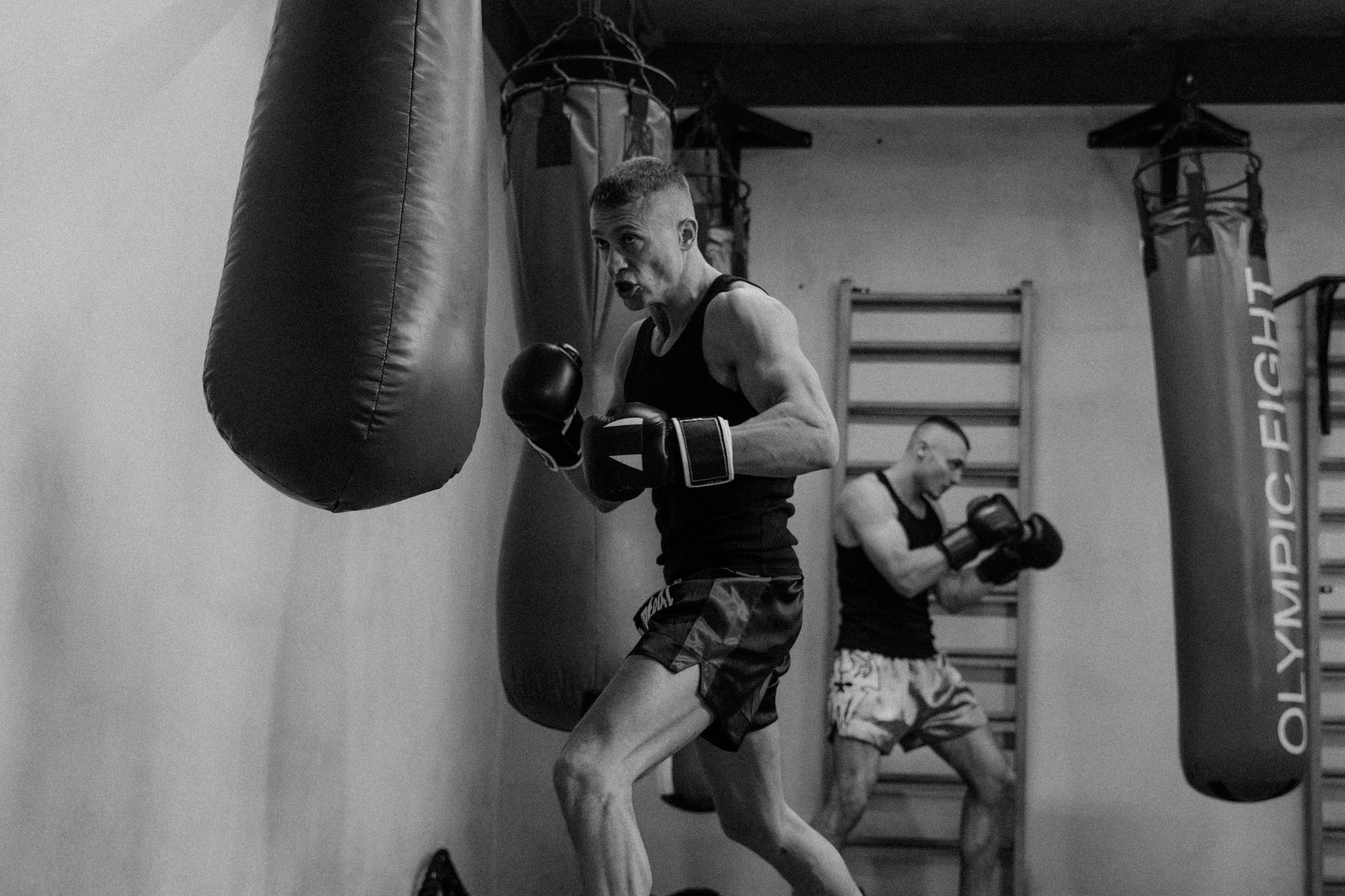 Athletes practicing boxing in a gym, showcasing dynamic movement and focus in black-and-white.